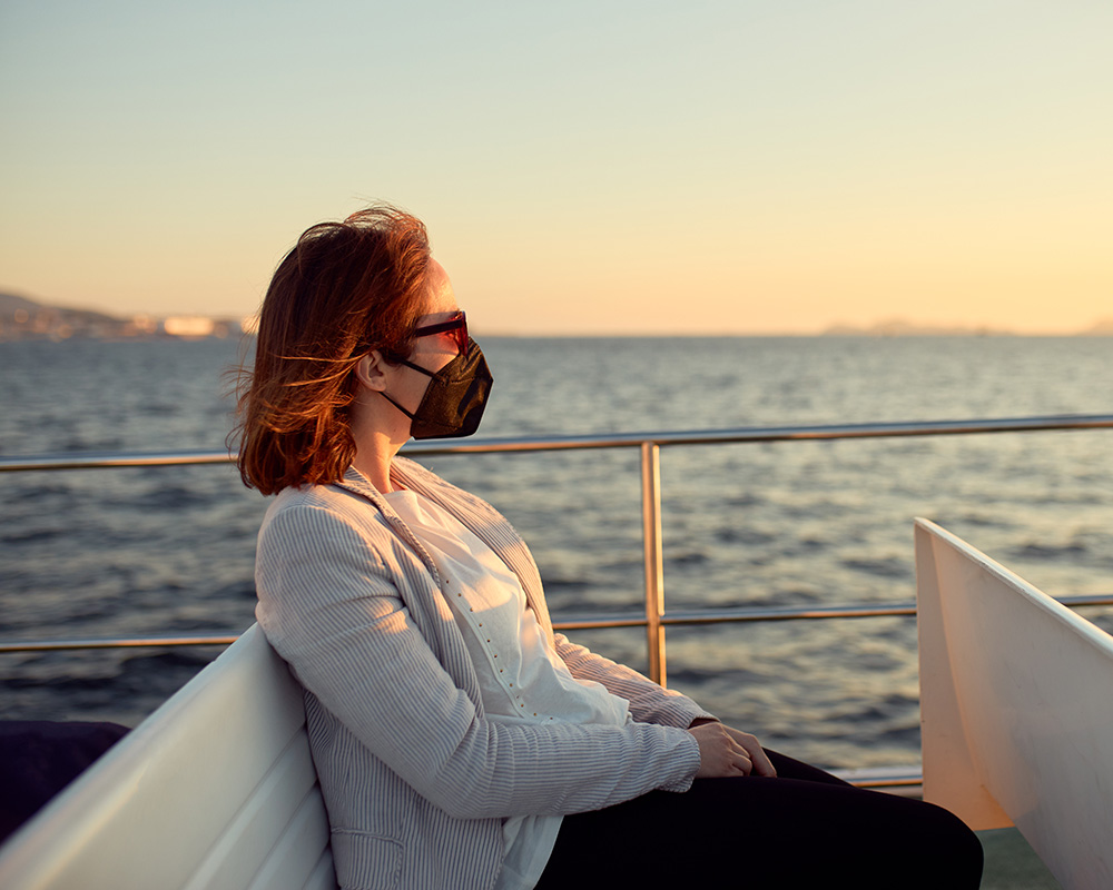 Mujer con mascarilla y gafas de sol sentada en una barco